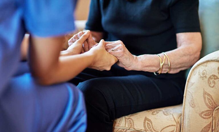 Older adult and family member review care costs, benefit paperwork, and a household budget at a kitchen table